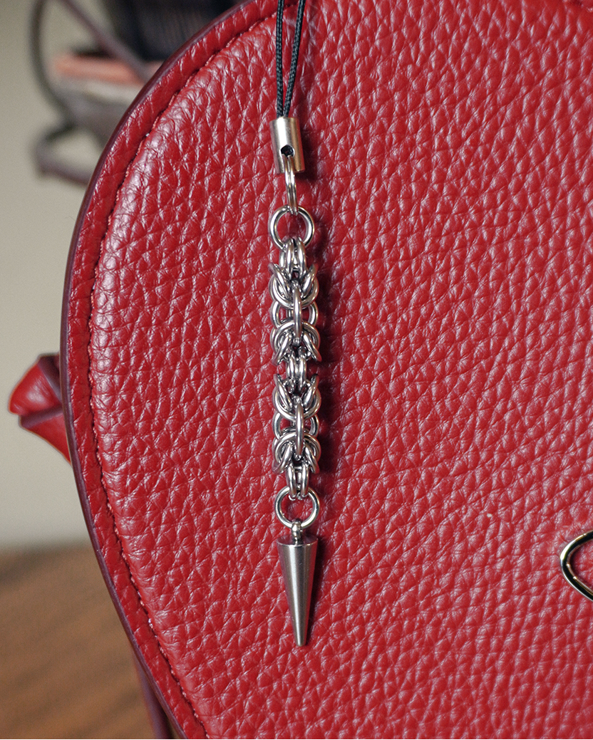 a spiky chainmail phone charm hanging against a red handbag.