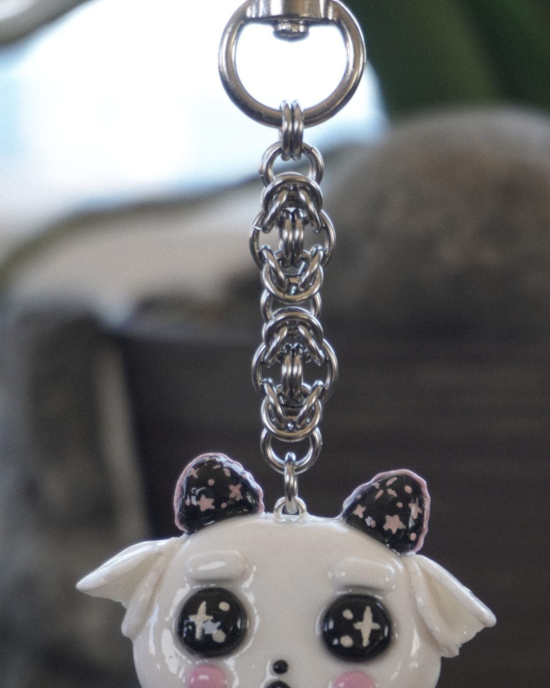 A close-up of stainless steel keychain featuring a white cartoon goat face with large black eyes, pink cheeks, and black and pink star-patterned ears, attached to a stainless steel silver chain and heart keychain clasp.