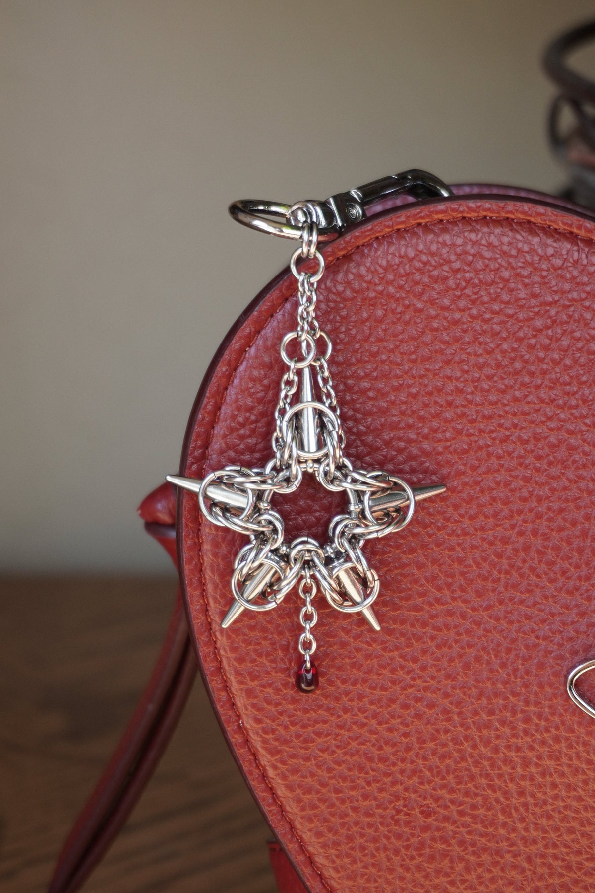 stainless steels silver toned chainmail star pendant keychain with a red glass bead hanging from it against a red heart bag